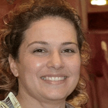 a woman with curly hair is smiling and wearing earrings