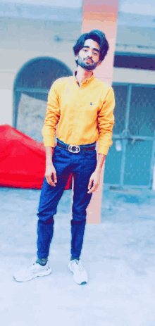 a young man wearing a yellow shirt and blue pants poses for a photo