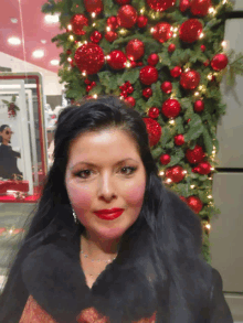 a woman stands in front of a christmas tree