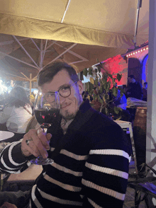 a man in a black and white striped sweater holds a glass of wine