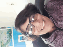 a woman wearing glasses and a purple sweater smiles