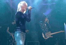 a man sings into a microphone while another man plays a guitar in front of a sign that says bbc four