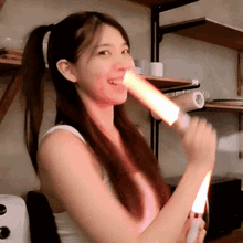 a woman in a white tank top holds a red light stick in her mouth