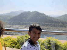 a young boy stands in front of a railing with mountains in the background and a sign that says ' state of india '