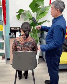 a man is brushing a woman 's hair while she sits in a chair with a plant in the background