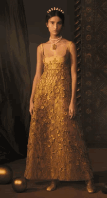 a woman wearing a gold dress and pearls is standing in front of some gold balls