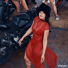 a woman in a red dress stands in front of a motorcycle