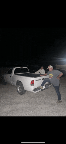 a man standing next to a white dodge truck at night