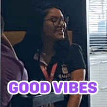 a woman wearing glasses and a shirt that says queen smiles in front of a sign that says " good vibes "