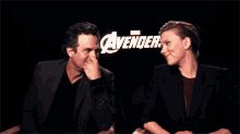 a man and a woman are sitting in front of a sign that says ' avengers '