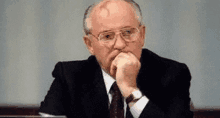 a man in a suit and tie is sitting at a desk with his hands on his chin .