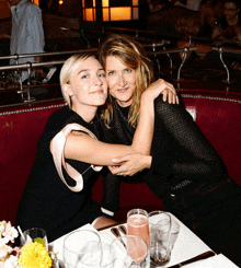 two women are posing for a picture while sitting at a table with drinks