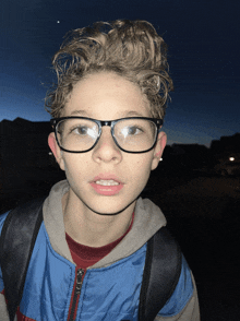 a boy wearing glasses and a backpack looks at the camera