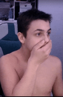 a shirtless man covering his mouth with his hands