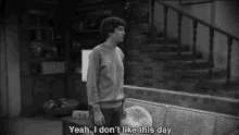 a black and white photo of a man standing next to a couch with the words yeah i don 't like this day below him