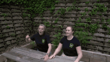 two women sitting at a picnic table with one wearing a shirt with a chef 's crown on the front