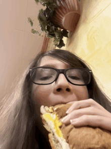 a woman wearing glasses is eating a sandwich with her eyes closed