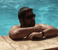 a shirtless man wearing sunglasses is leaning on the edge of a swimming pool