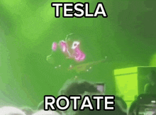 a man is playing a guitar in front of a crowd and the words tesla rotate are on the screen .