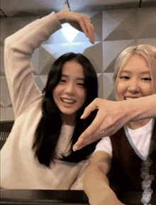 two women are making a heart shape with their hands while sitting at a table .