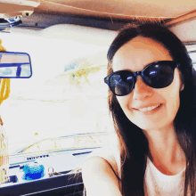 a woman wearing sunglasses and a white shirt smiles in a car