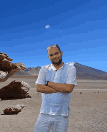 a man in a white shirt stands with his arms crossed in front of a mountain