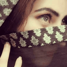 a close up of a woman covering her face with a floral scarf .