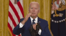 a man in a suit and tie is giving a speech in front of a microphone in front of an american flag .