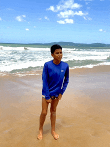 a boy in a blue shirt stands on a sandy beach