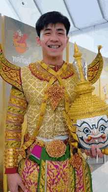 a man in a costume holds a mask in front of a sign that says ' thailand ' on it