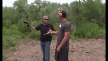 two men are standing in a field talking to each other while one of them is holding a gun .