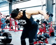 a man is lifting a dumbbell in a gym while wearing a black tank top with the number 5 on it .