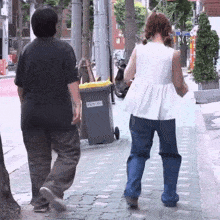 a man and a woman are walking down a sidewalk next to a trash can that says ' seoul ' on the side