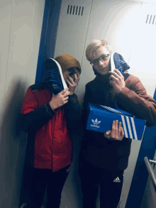 two boys holding up their shoes and a blue adidas box