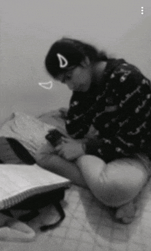 a black and white photo of a girl sitting on the floor looking at her phone