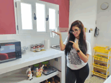 a woman standing in a kitchen pointing at a microwave