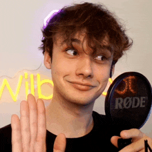 a young man is holding a rode microphone in front of a neon sign that says wilb