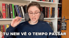 a woman wearing glasses stands in front of a bookshelf with a sign that says " tu nem ve o tempo passar "