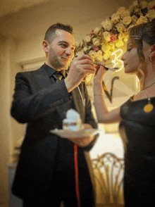 a man in a black suit is feeding a woman a piece of cake