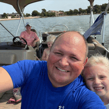 a man wearing a blue under armour shirt takes a selfie with two children on a pontoon boat