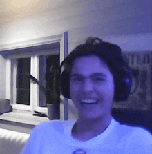 a young man wearing headphones and a white shirt is smiling in a dark room .