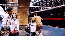 a group of people are standing in front of a train station with the number 9 on the sign .