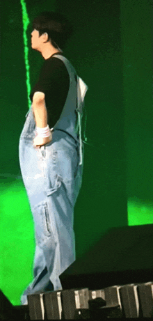 a man wearing overalls is standing on a stage with a green background