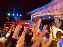 a crowd of people holding up red cups with a man wearing a shirt that says ' arizona ' on it