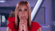 a woman in a red shirt is praying with her hands folded in front of a sign that says global