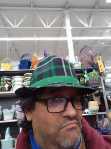 a man wearing glasses and a green plaid hat stands in front of a shelf with baskets