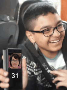 a boy with glasses is holding a cell phone with the number 31 on it