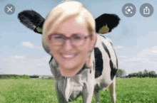 a woman with glasses is standing in a field with a cow 's head .