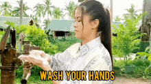 a woman is washing her hands in front of a water pump with the words `` wash your hands '' .