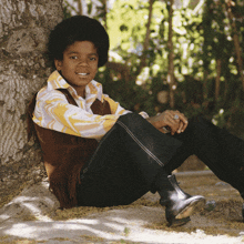 a young boy leans against a tree while wearing a fringed vest